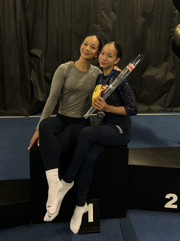 Lia and Olivia sit together on the top of a podium